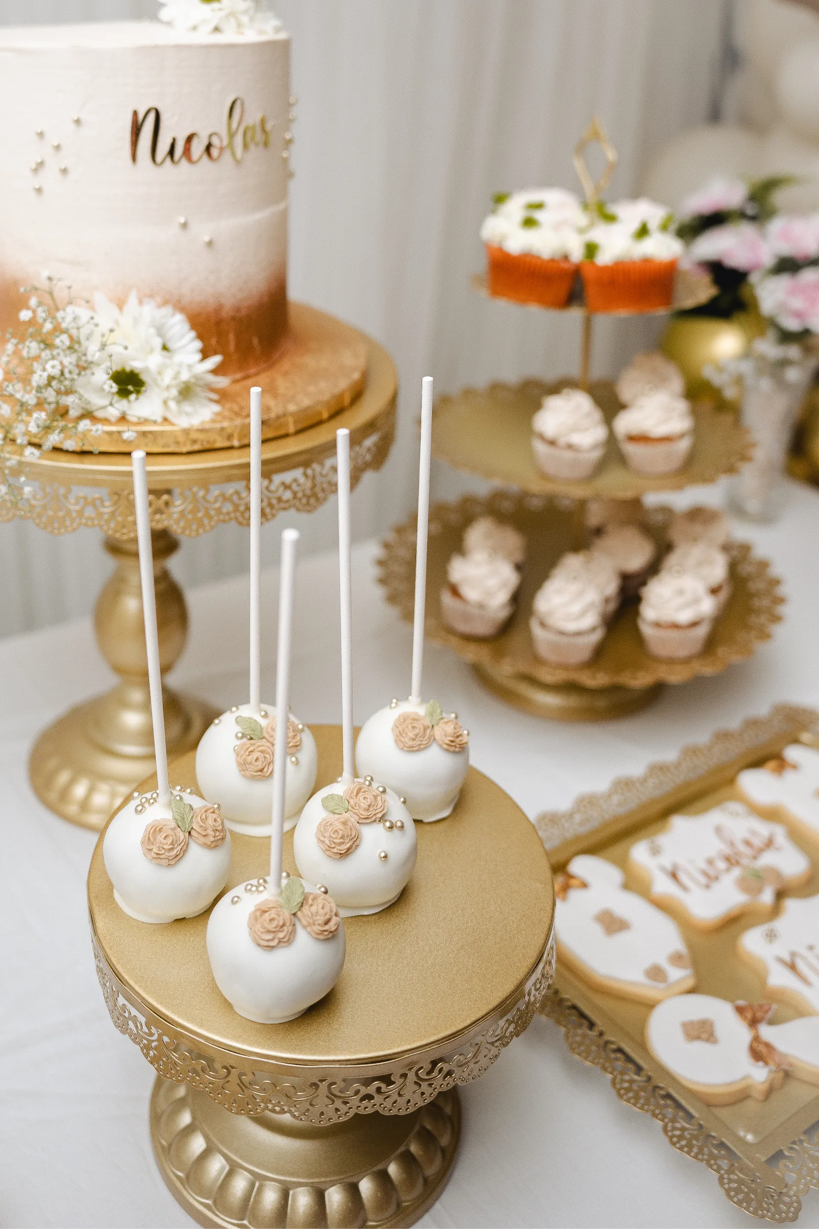 Tarta con nombre escrito en dorado, junto a cake pops de flores